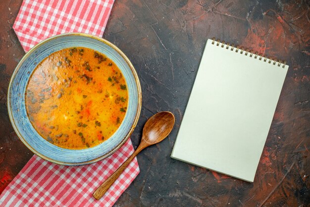 Draufsicht Reissuppe in Schüssel auf rot-weiß kariertem Tischtuch Holzlöffel Notizblock auf Hintergrund