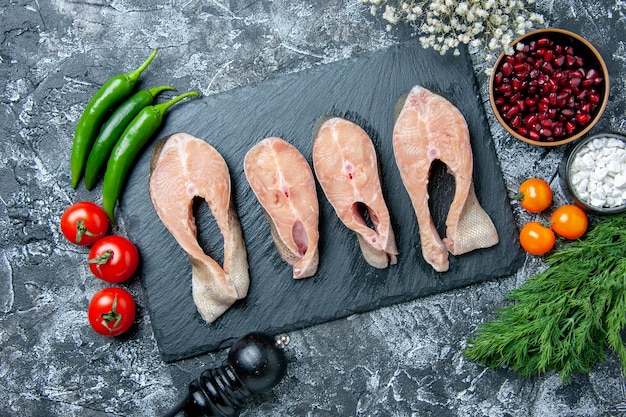 Draufsicht rohe Fischscheiben auf schwarzem Brett Pfeffermühle Gemüse kleine weiße Blumen auf dem Tisch