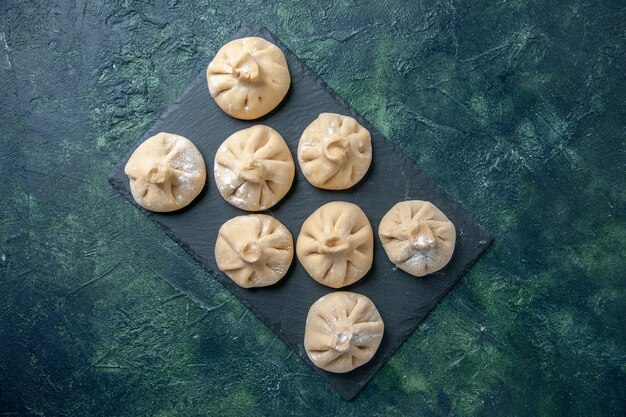 Draufsicht rohe kleine Knödel mit Fleisch innen auf dunklem Oberflächenfarbgericht, das Mahlzeitteigfleischmehl kocht