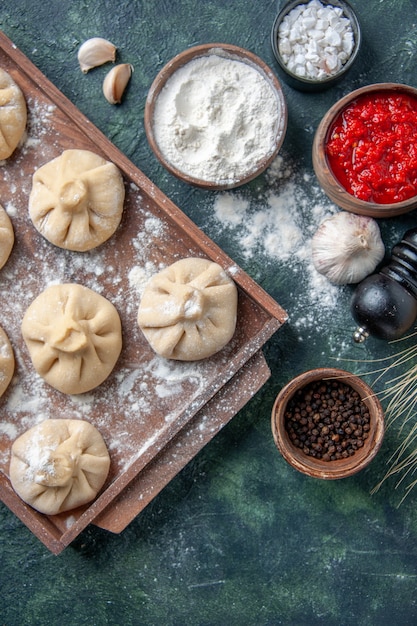 Draufsicht rohe kleine Knödel mit Fleisch innen auf dunklem Oberflächenfarbmahlzeitgericht, das Mehlfleisch kocht