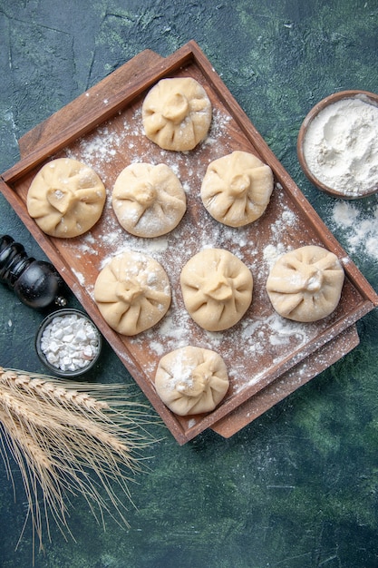 Draufsicht rohe kleine Knödel mit Fleisch innen auf einem dunklen Oberflächenfarbenmahlzeitgericht, das Mehlteigfleisch kocht