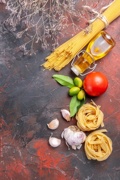 Draufsicht rohe Nudeln mit Öl und Tomaten auf der dunklen Oberfläche rohe Teignudeln