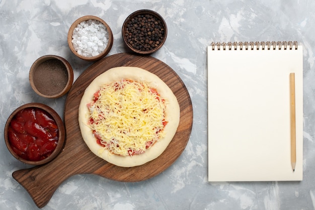 Draufsicht rohe Pizza mit Käsegewürzen auf Weiß