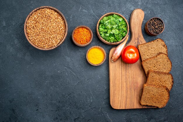 Draufsicht roher Buchweizen mit Grüns und Brotlaiben auf dunkelgrauem Raum