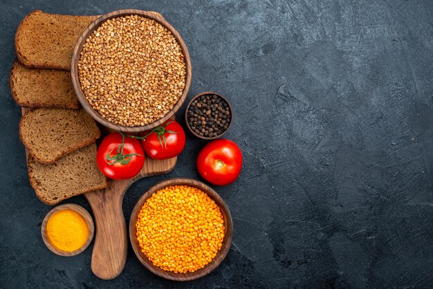 Draufsicht roher Buchweizen mit Tomaten und Brotlaiben auf dunkelgrauem Raum