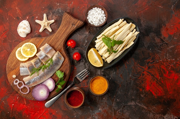 Draufsicht roher geschnittener Fisch mit Zwiebelringen und Gewürzen auf dunklem Hintergrund