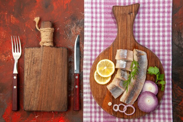 Draufsicht roher geschnittener Fisch mit Zwiebelringen und Zitrone auf dunklem Hintergrund