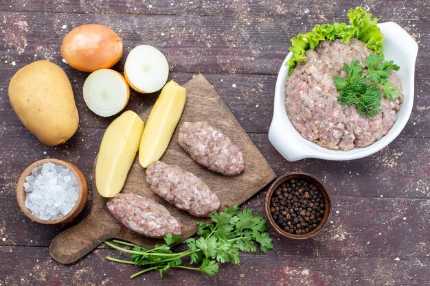 Draufsicht rohes Fleisch mit rohen Kartoffeln Salz Zwiebel Notizblock und Gemüse auf dem braunen Holz Schreibtisch Fleisch Kartoffel Gericht Mahlzeit Abendessen