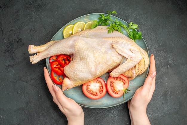 Draufsicht rohes frisches Huhn innerhalb des Tellers mit Grüns und Gemüse auf dunklem Hintergrund