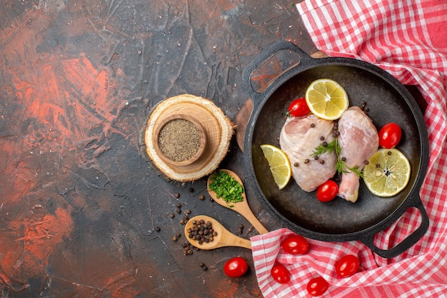 Draufsicht rohes Huhn mit Zitrone und Kirschtomaten in der Pfanne auf dunklem Hintergrund