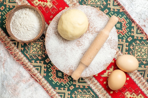 Draufsicht rohes Teigstück mit Mehl auf dem bunten Teppich und weißem Hintergrundmehl backen Teig