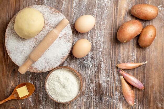 Draufsicht rohes Teigstück mit Mehlkartoffeln und Eiern auf hölzernem Schreibtischmehlbackteig