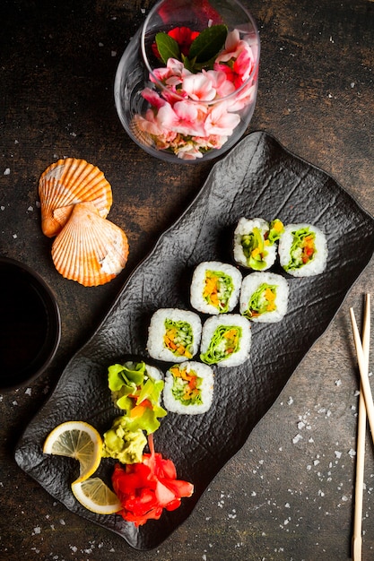 Draufsicht Rollensatz mit eingelegtem Ingwer und Wasabi und Sojasauce und Stäbchen in dunklem Teller