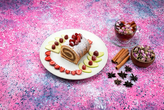 Kostenloses Foto draufsicht rollkuchen innenplatte mit äpfeln und erdbeeren zusammen mit zimt und tee auf dem farbigen schreibtischkuchen keks backteig schokolade