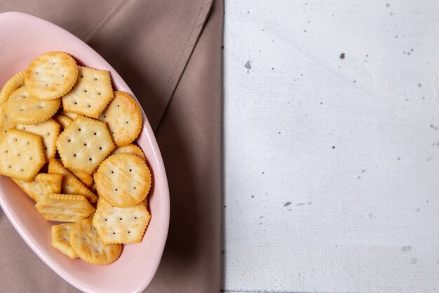 Draufsicht rosa Platte mit Crackern auf dem weißen Hintergrundplätzchensnack knuspriger Cracker