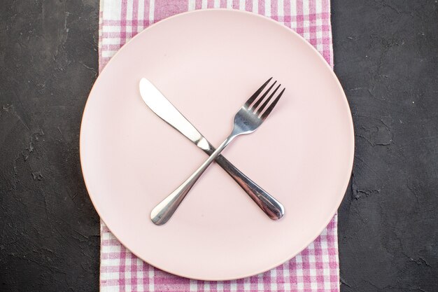 Draufsicht rosa Platte mit Gabel und Messer auf dunklem Hintergrund