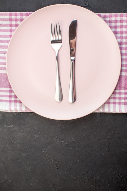 Draufsicht rosa Platte mit Gabel und Messer auf dunklem Hintergrund