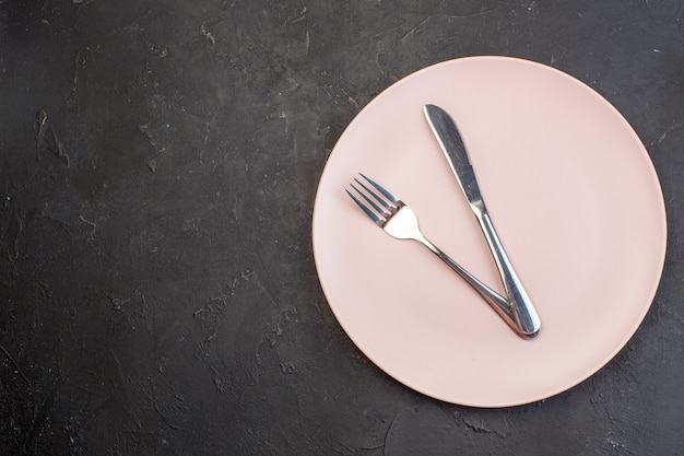 Draufsicht rosa Platte mit Gabel und Messer auf dunkler Oberfläche