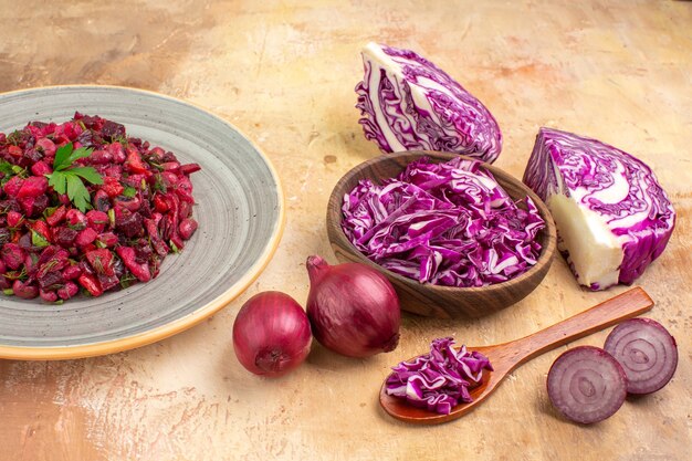 Draufsicht Rote-Bete-Salat auf einer Keramikplatte mit roten Zwiebeln und einer Schüssel mit gehacktem Rotkohl auf Holzhintergrund