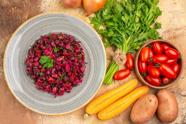 Draufsicht Rote-Bete-Salat auf einer Keramikplatte und Zutaten für die Zubereitung auf Holzhintergrund