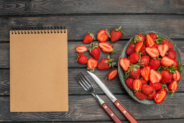 Draufsicht rote Erdbeeren in Scheiben geschnitten und ganze Früchte auf dunklem rustikalem Schreibtisch aus Holz