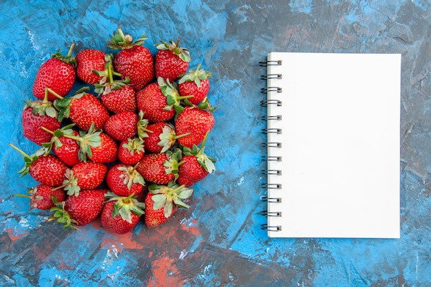 Kostenloses Foto draufsicht rote erdbeeren mit notizblock auf blauem hintergrund