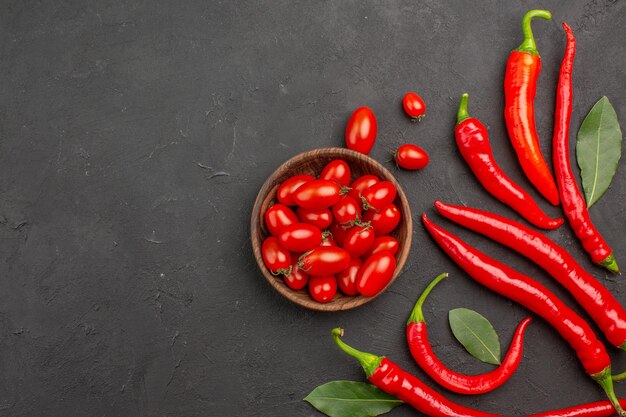 Draufsicht rote Paprika und Lohnblätter und eine Schüssel Kirschtomaten auf der rechten Seite des schwarzen Tisches mit freiem Platz