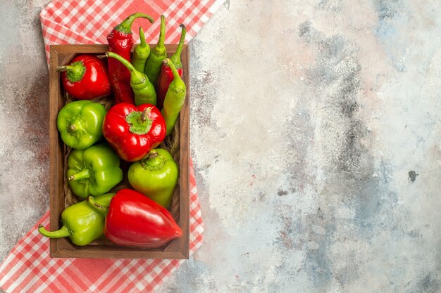 Draufsicht rote und grüne Paprikaschoten Peperoni in der Holzkiste auf karierter Tischdecke auf nacktem oberflächenfreiem Platz