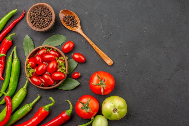 Draufsicht rote und grüne Paprikaschoten und eine Schüssel Kirschtomaten schwarzer Pfeffer und rote und grüne Tomaten auf der linken Seite der schwarzen Oberfläche