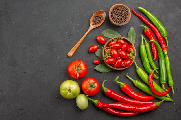 Draufsicht rote und grüne Paprikaschoten und eine Schüssel Kirschtomaten schwarzer Pfeffer und rote und grüne Tomaten auf der rechten Seite der schwarzen Oberfläche