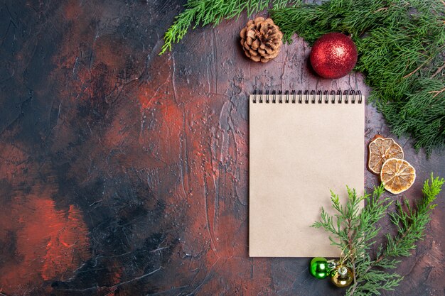 Draufsicht roter Stift ein Notizbuch Kiefernzweige Weihnachtsbaumballspielzeug getrocknete Zitronenscheiben eine Tasse Tee auf dunkelroter Oberfläche Freiraum Weihnachtsfoto