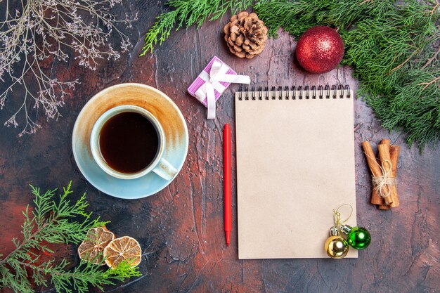 Draufsicht roter Stift ein Notizbuch Kiefernzweige Weihnachtsbaumballspielzeug Zimtstangen eine Tasse Tee auf dunkelroter Oberfläche Weihnachtsfoto