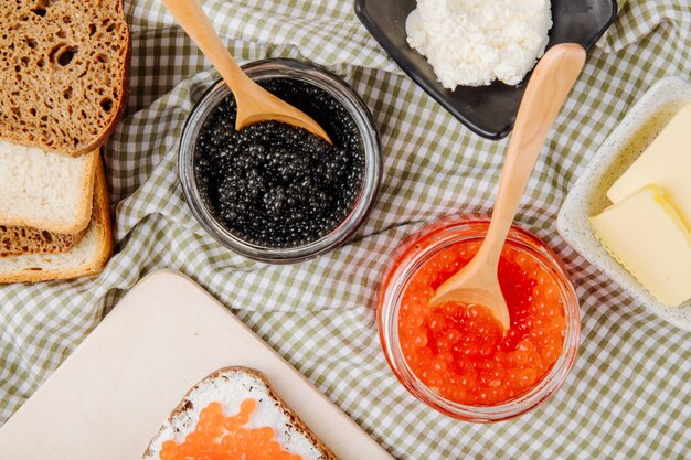 Draufsicht rotes und schwarzes Kaviarglas mit Roggenbrot-Weißbrotbutter und Hüttenkäse auf dem Tisch