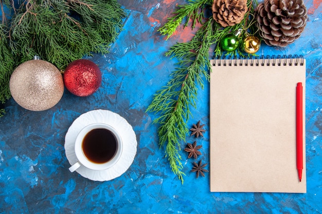 Draufsicht Rotstift auf einem Notizbuch Kiefernzweige Weihnachten verziert eine Tasse Tee auf blauer Oberfläche