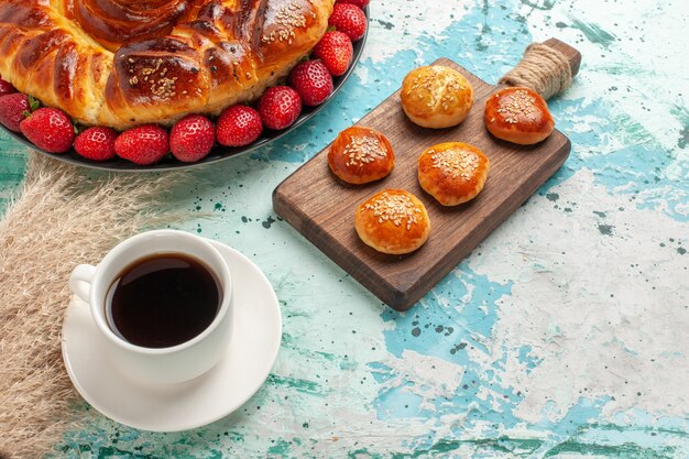 Draufsicht runde köstliche Torte mit Erdbeeren und Tasse Tee auf hellblauer Oberfläche