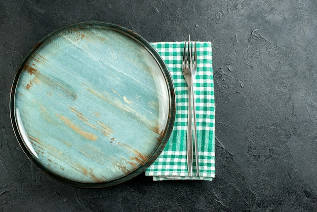 Kostenloses Foto draufsicht runde platte abendessen messer und gabel auf grün und weiß karierte serviette auf schwarzer oberfläche freien raum