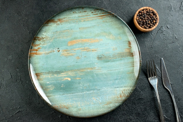 Kostenloses Foto draufsicht runde platte abendessen messer und gabel schwarzer pfeffer in schüssel auf schwarzem tisch