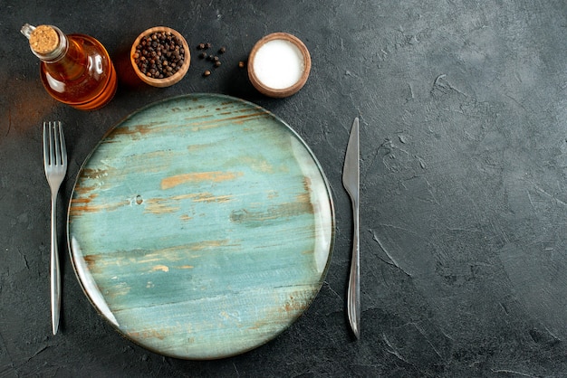 Draufsicht runde platte abendessen messer und gabel schwarzer pfeffer und salzöl flasche auf schwarzem tisch mit freiem platz