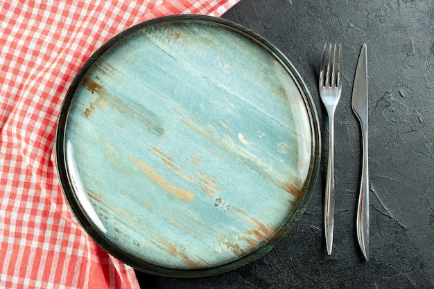Draufsicht runde Platte Stahlgabel und Abendessenmesser rot und weiß karierte Tischdecke auf schwarzem Tisch