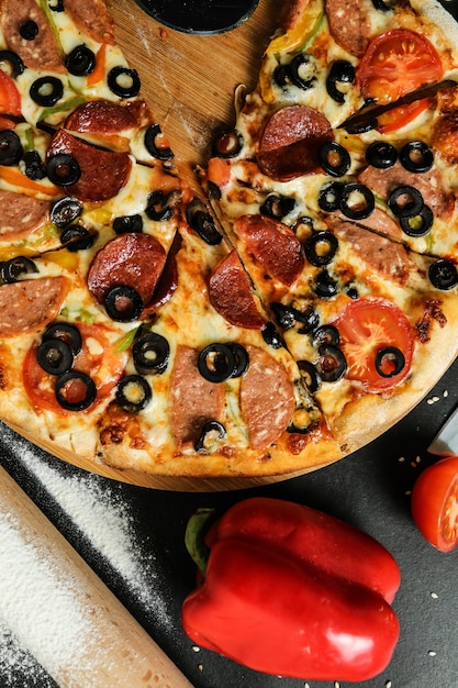 Draufsicht Salami-Pizza auf Stand mit Tomatenoliven und Paprika auf schwarzem Tisch