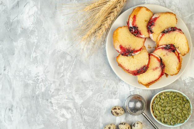 Draufsicht Scheiben Marmeladenkuchen auf Teller Kürbiskerne in Schüssel Weizenspitzen Wachteleier auf Tisch mit freiem Platz
