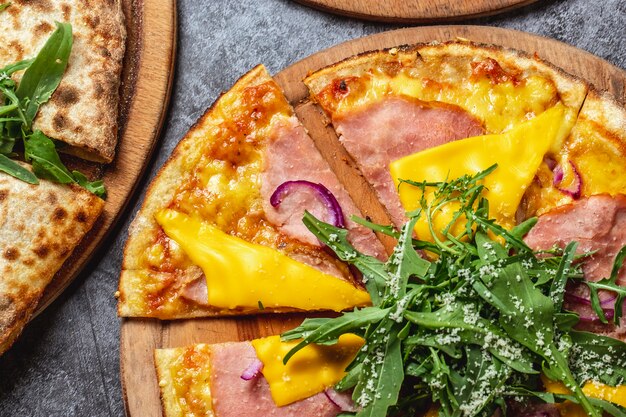 Draufsicht Schinken und Käsepizza mit geschmolzenem Käseparmesan und Rucola auf einem Brett