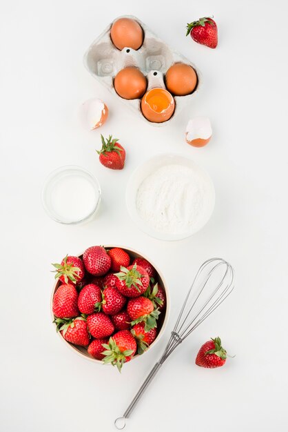 Draufsicht Schneebesen mit Erdbeeren und Eiern