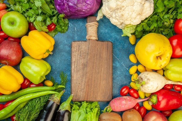 Draufsicht Schneidebrett Kirschtomaten Cumcuat Quitte Äpfel Auberginen Rettich Koriander Rotkohl Blumenkohl auf blauem Tisch