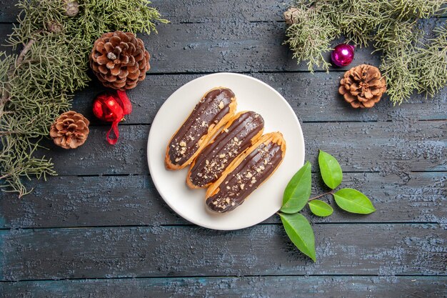 Draufsicht Schokoladen-Eclairs auf einem ovalen Tellerkegelweihnachtsspielzeug-Tannenbaumblätter auf dunklem Holzgrund mit freiem Raum