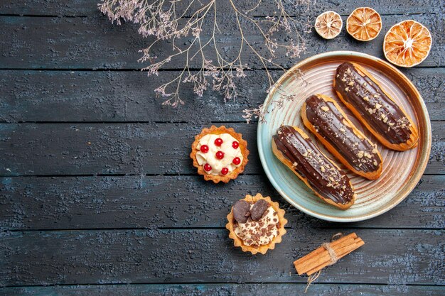 Kostenloses Foto draufsicht schokoladen-eclairs auf ovalem teller getrockneten blumenzweigtörtchen zimt und getrocknete orangen auf dem dunklen holzgrund mit kopierraum