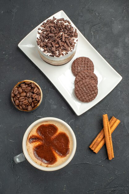 Draufsicht Schokoladenkuchen und Kekse auf weißer rechteckiger Teller Tasse Kaffee Zimtstangen Schüssel mit Kaffeesamen auf dunklem, isoliertem Hintergrund