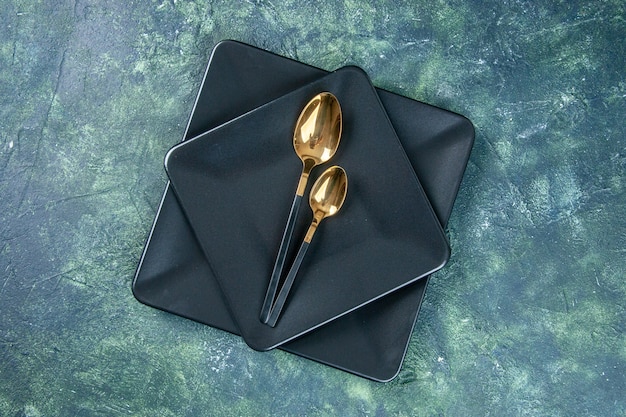 Draufsicht schwarze Teller mit goldenen Löffeln auf dunklem Hintergrund färbt Lebensmittelbesteckrestaurant-Abendessencafé