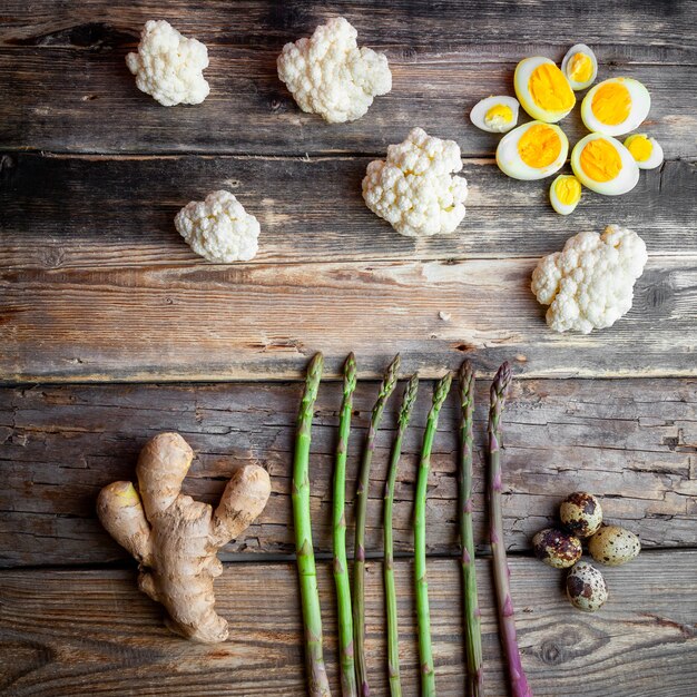 Draufsicht Spargel mit Ingwer, Eiern, Blumenkohl auf dunklem hölzernem Hintergrund.