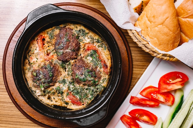 Draufsicht Spiegeleier mit Fleischbällchen und Kräutern in einer Pfanne Scheiben Tomaten und Gurke